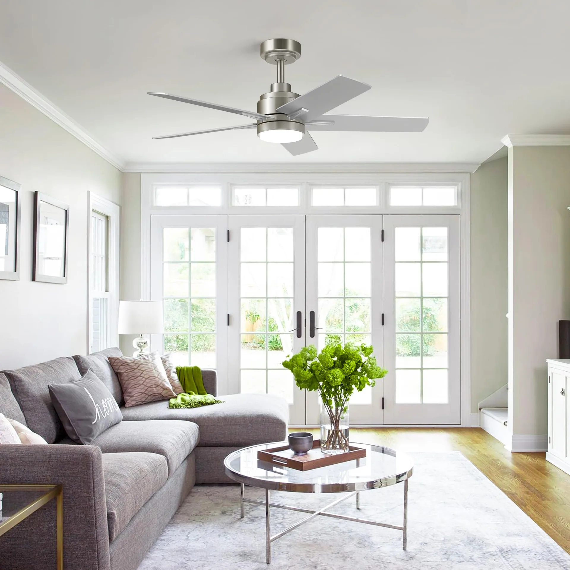 Bright living room with a brushed nickel ceiling fan and LED light above a grey sofa and round glass coffee table